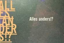Schriftzug "Alles anders?!" auf grauem Grund mit bunten Farbsprenkeln