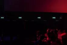 Bild in rot schwarzen Tönen auf dem ein Publikum auf eine große Kinoleinwand schaut