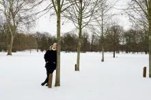 Person steht an Baum gelehnt in Schneelandschaft