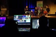 Blick auf das Podium auf der Bühne. Im Vordergrund die Aufnahmetechnik des Livestreamings