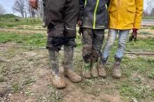 3 vermatschte Paare an Gummistiefeln vor den Beeten der Permagold-Fläche.