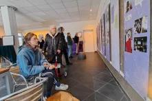 Eine Person schaut sich im Sitzen und mit Kopfhörern im Ohr ein Banner der Ausstellung "zusammentun" an. Im Hintergrund blicken weitere Personen stehend auf die Banner.
