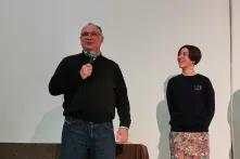 Ein Mann mit Brille spricht in ein Mikrofon, eine Frau hört lächelnd zu