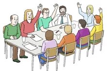 Menschen an einem Tisch. Über Handzeichen stimmen sie gerade ab.