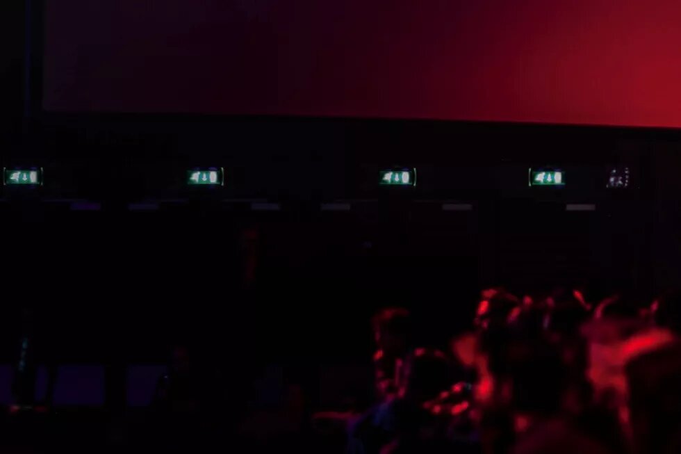 Bild in rot schwarzen Tönen auf dem ein Publikum auf eine große Kinoleinwand schaut