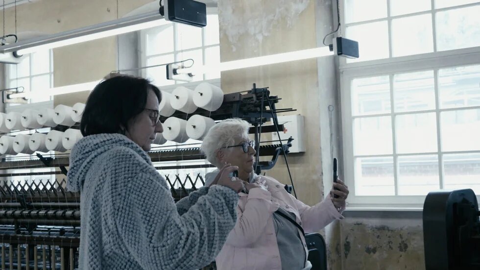 Zwei Frauen halten Spindel in der Textilfabrik in die Luft und sind darüber im Gespräch