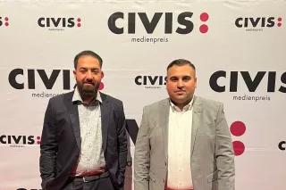 Die Podcaster Sejnur Memisi und Nino Novakovic stehen vor einem Banner des CIVIS Medienpreises, für den sie im Jahr 2022 nominiert sind.